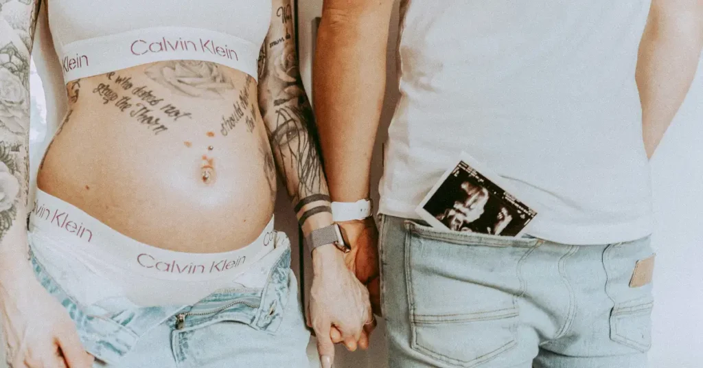 Pregnant woman with tattoo on belly holding hands with her husband